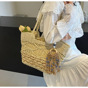 Close-up of woven straw tote bag with evil eye tassel and decorative tulips on a model