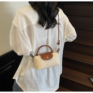 Detailed view of handmade woven straw handbag with brown leather flap on white linen outfit