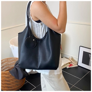 Détail du sac cabas en cuir noir grainé avec un pendentif décoratif rond élégant