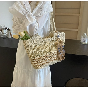Detail of woven straw tote bag with evil eye tassel charm and hollow mesh texture