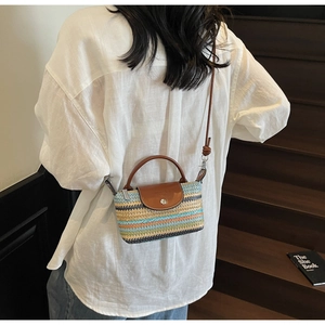 Detail of hand-woven straw crossbody bag featuring multi-color stripes and leather flap