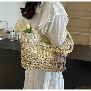 Detail of hand-woven straw tote bag with wave pattern and evil eye tassel charm