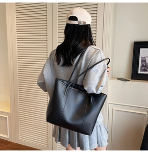 Detailed view of a black leather tote bag with shoulder straps worn in a bright room