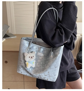 Silver tote bag with numeric print, metal logo, and plush bear charm on shoulder