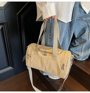 Detail of beige nylon travel bag with silver zippers and adjustable strap held by model