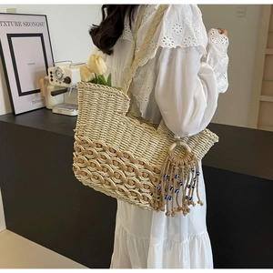 Close-up of a woven straw tote bag with a blue beaded tassel charm and woven handle