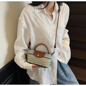 Detail of a mini hand-woven straw crossbody bag with multi-colored stripes and leather flap