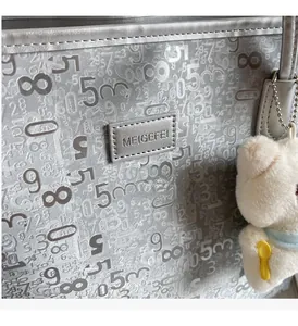 Close-up of silver tote bag with digital prints, metal logo and a plush bear charm