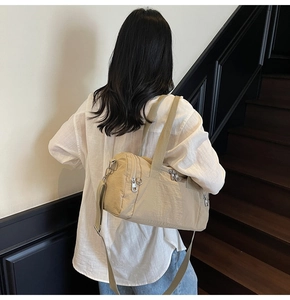 Detail of beige nylon travel bag showing adjustable shoulder strap and metal zippers