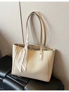 Large beige woven tote bag with decorative scarf and zipper on a black leather seat