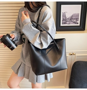 Detail of matte black leather tote bag with subtle gold logo and slim shoulder straps