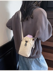 Minimalist beige nylon bucket bag with drawstring closure and purple bottle accessory