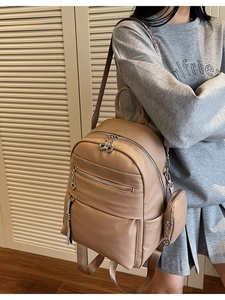 Minimalist khaki leather backpack with multi-zippers and mini round bag charm on model
