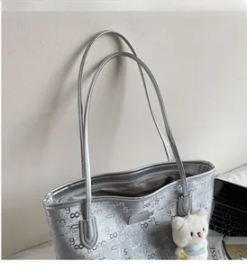 Detailed view of silver embossed tote bag with plush bear charm and metallic brand logo