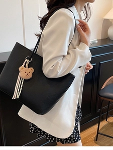 Large black pebbled leather tote bag with plush bear charm worn by a model in a suit