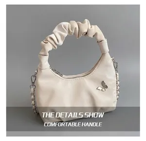 Détail du sac à main blanc crème avec poignée plissée et breloque papillon argentée