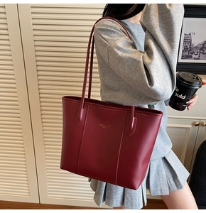 Detail of burgundy leather tote bag with gold logo shown on model for size reference