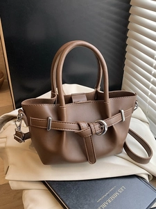 Sac seau en simili cuir marron avec plis et boucle métallique sur un bureau ensoleillé