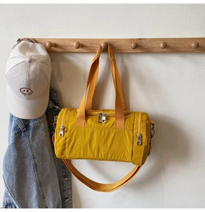 Yellow nylon travel bag hanging with baseball cap and denim jacket on wood wall