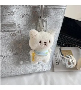 Detail of white plush cat charm with blue scarf on silver mirror tote bag