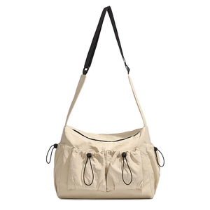 Detail of beige nylon crossbody bag with large drawstring pockets and adjustable black strap