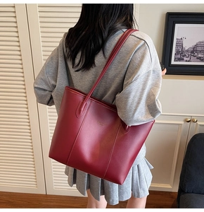 Macro view of burgundy matte leather tote bag with gold lettering and slim shoulder straps