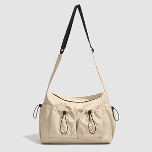Detail of beige nylon tote bag featuring front drawstring pockets and black strap