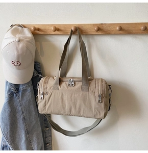 Detail of a beige nylon cylinder travel bag hanging on a hook with a baseball cap