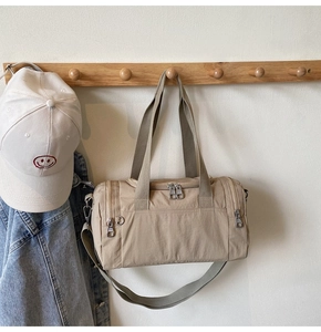 Minimalist beige nylon travel bag with metal zippers hanging on a wooden rack