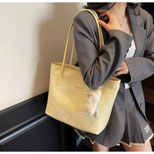 Detail of light yellow tote bag with embossed texture and a cute white bear pendant