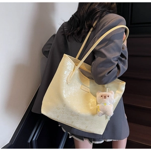 Detail of pale yellow leather tote with letter patterns and plush bear charm