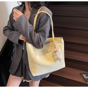 Detail of light yellow patent leather tote bag with embossed pattern and bear charm
