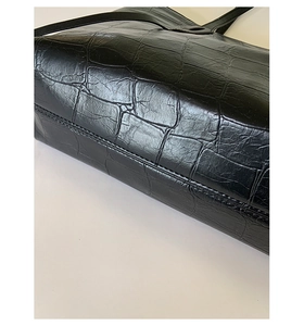 Close-up of black crocodile embossed leather tote showing fine stitching and glossy texture