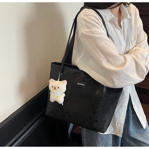 Detailed side view of black large capacity leather tote bag with pattern and bear charm