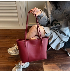 Detail of burgundy leather tote bag with vertical stitching and gold Fashion Trend lettering