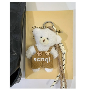 Detail of white plush bear keychain with brown corduroy overalls on a textured bag