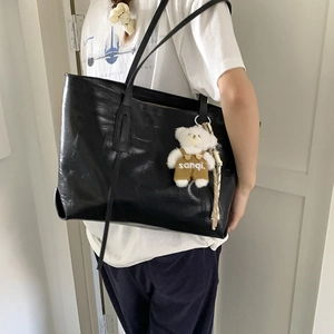 Detail of a large black leather tote bag with slender straps and a plush bear pendant