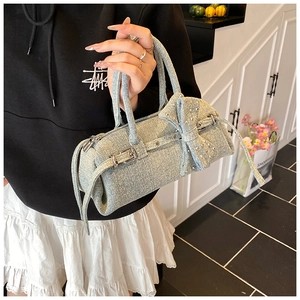 Detail of light blue denim Boston bag with oversized bow and silver rivets on the surface