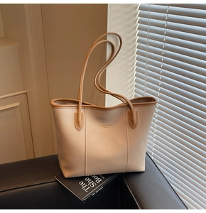 Detail of cream tote bag with brown trim and long shoulder straps on a leather sofa