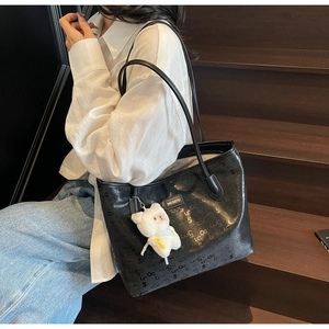 Detailed shot of large black printed tote bag with a white plush bear charm on wood stairs