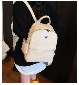 Détail d'un mini sac à dos beige texturé avec un badge métallique triangulaire logo
