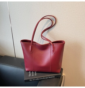 Close-up of a burgundy leather tote bag with elegant gold brand logo on surface