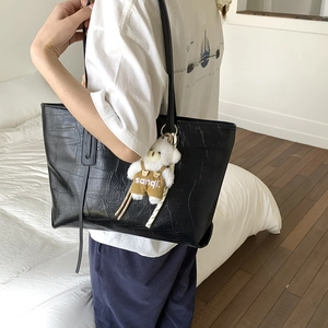 Detail view of large black crocodile embossed tote bag with a cute plush bear charm accessory