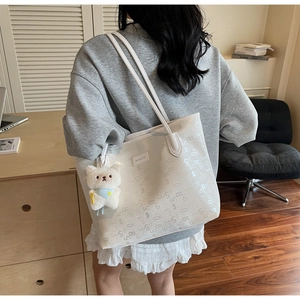 Detail of white tote bag with silver numeric print and plush bear charm on strap