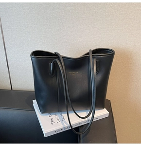 Detail of minimalist black leather tote bag featuring a textured finish and shoulder straps