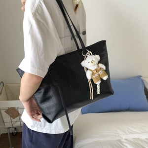 Detail of black crocodile texture tote bag with a cute bear charm in a lifestyle setting
