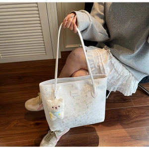 Detail of white tote bag with gray numbers, logo patch and plush bear accessory