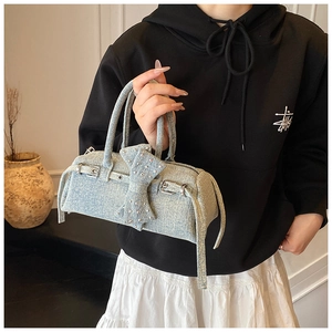 Detail of light blue denim pillow bag featuring a rivet bow and silver buckle accents