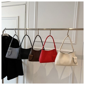 Close-up of assorted woven shoulder bags in five colors hanging on a metal rack