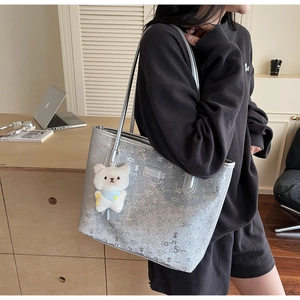 Detail of silver tote bag with numeric pattern, brand logo, and a plush bear charm